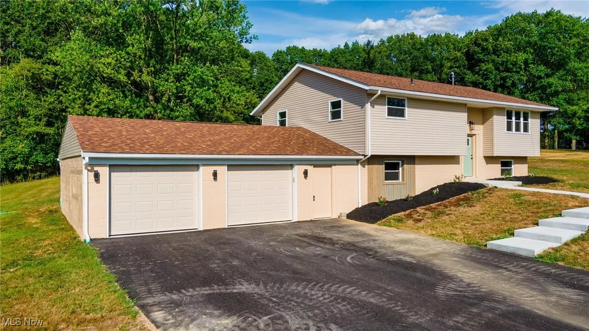 View of side of home with driveway, an attached garage, a lawn, and roof with shingles