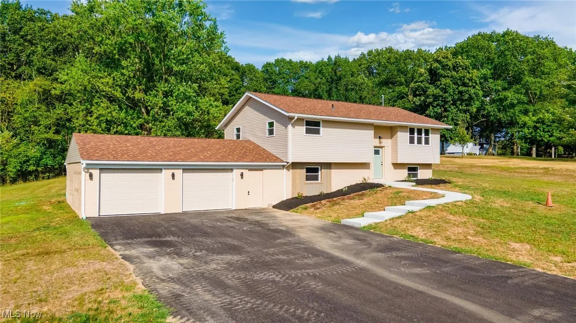 Raised ranch with a front lawn, an attached garage, asphalt driveway, and roof with shingles