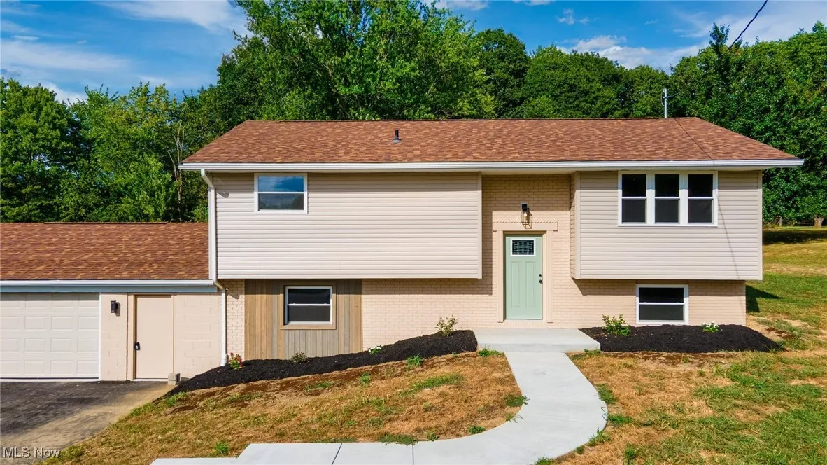 Bi-level home with brick siding, an attached garage, roof with shingles, and a front yard