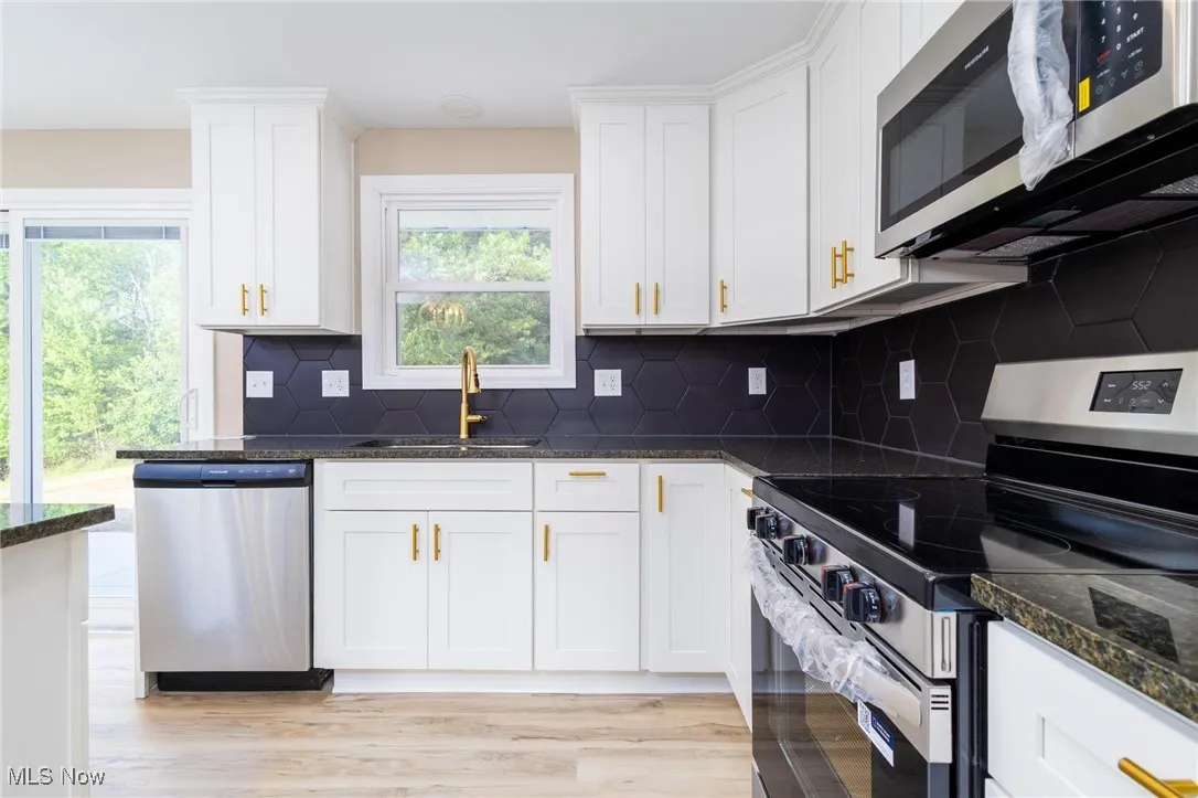 Kitchen with appliances with stainless steel finishes, white cabinetry, light wood-style flooring, backsplash, and dark stone​​‌​​​​‌​​‌‌​‌‌​​​‌‌​‌​‌​‌​​​‌​​ counters