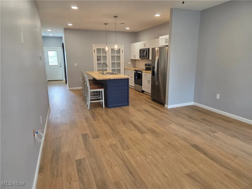 Kitchen featuring white cabinets, a kitchen island with sink, a breakfast bar area, appliances with stainless steel finishes, and decorative light fixtures
