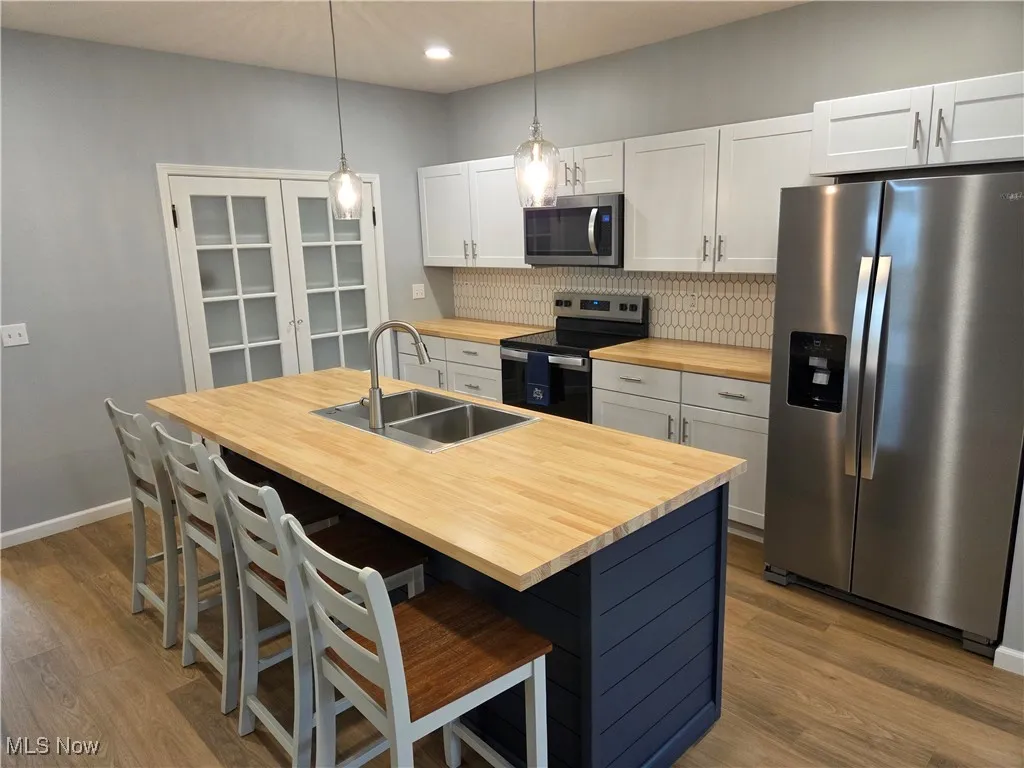 Kitchen featuring appliances with stainless steel finishes, decorative backsplash, an island with sink, hanging light fixtures, and a breakfast bar