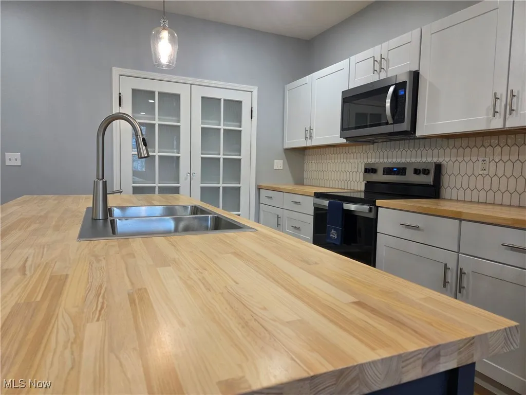 Kitchen featuring stainless steel appliances, pendant lighting, french doors, white cabinetry, and wood counters