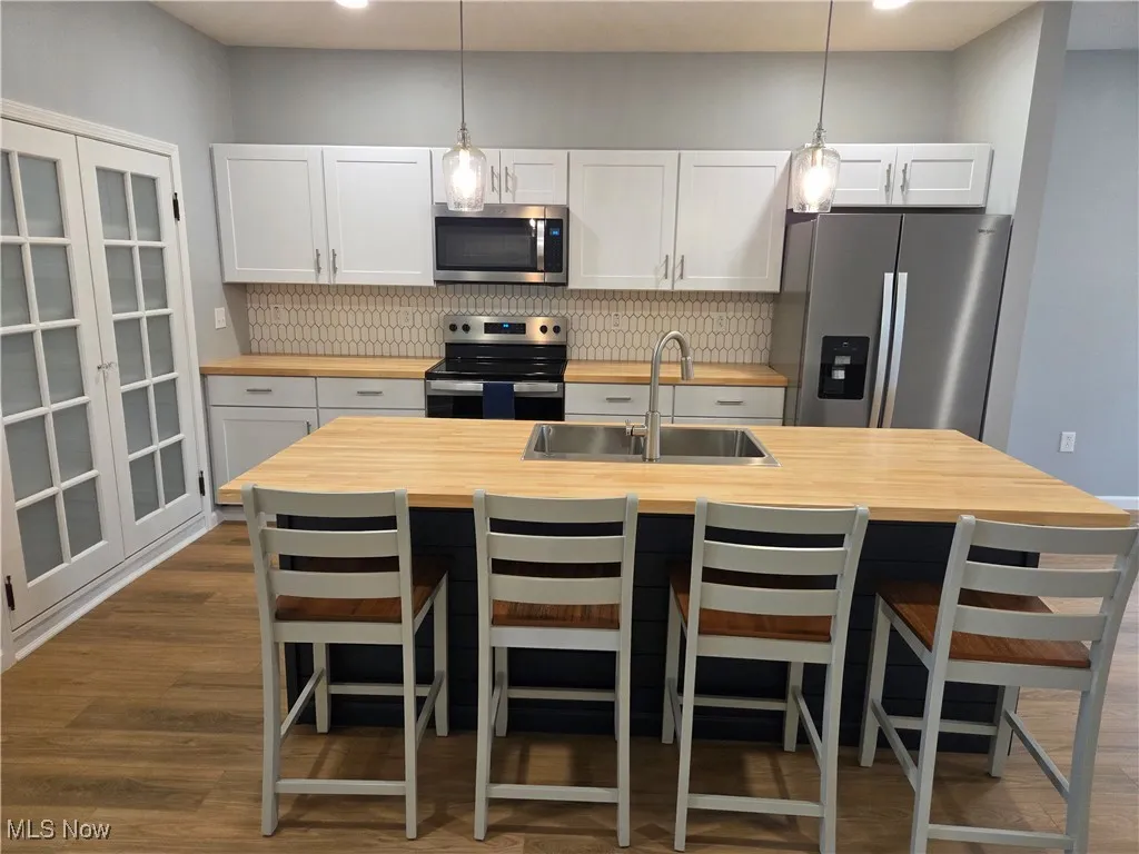 Kitchen with stainless steel appliances, a center island with sink, hanging light fixtures, white cabinets, and recessed lighting