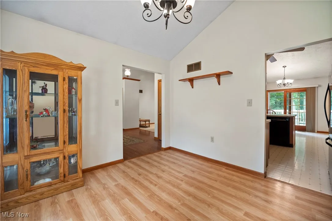 Empty room with a chandelier, light floors, and high vaulted ceiling