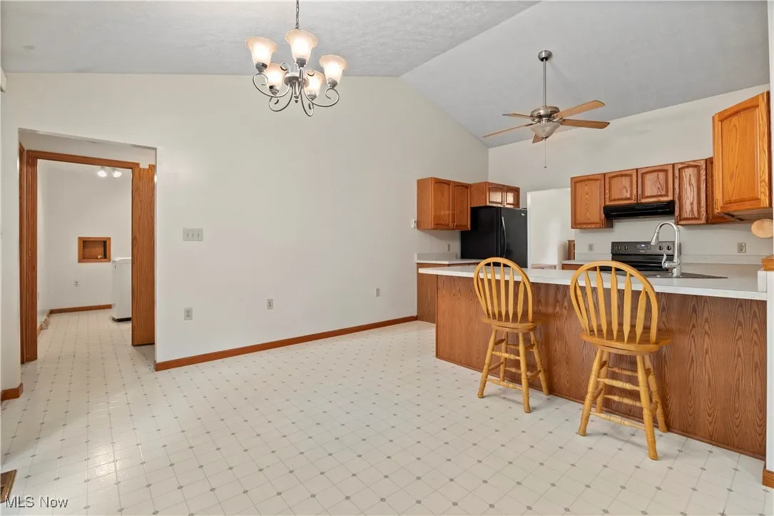 Kitchen with light countertops, brown cabinetry, decorative light fixtures, black appliances, and high vaulted ceiling