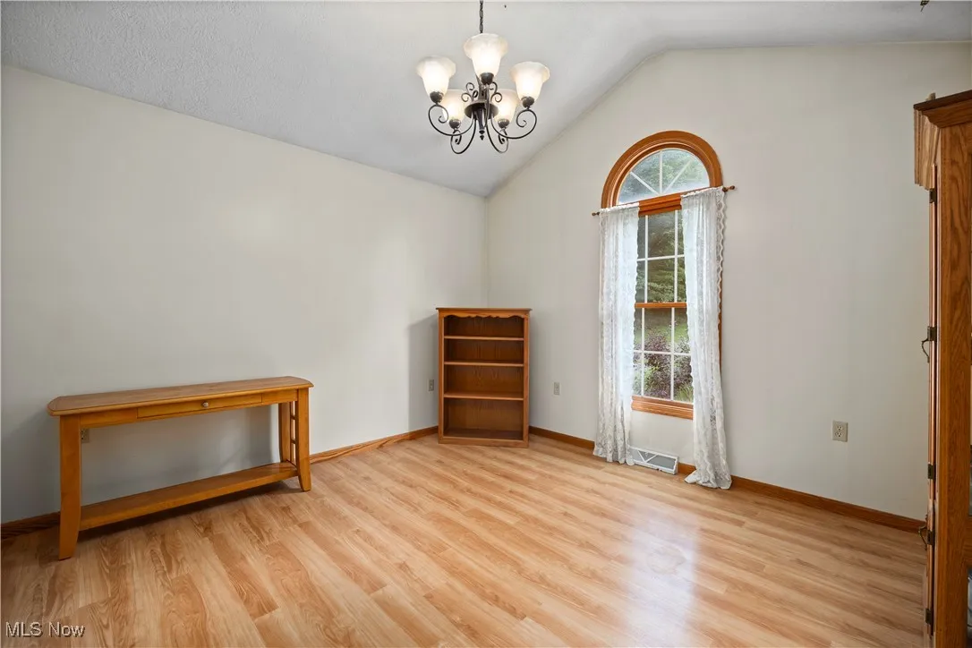 Unfurnished room featuring vaulted ceiling, light flooring, and a chandelier