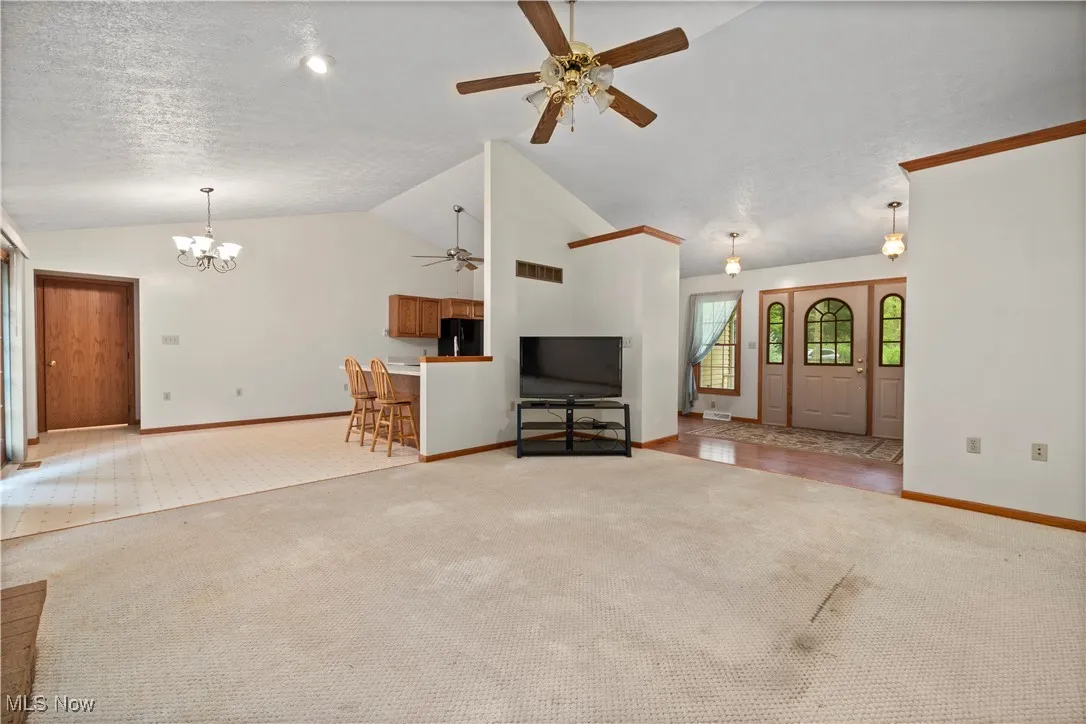 Unfurnished living room featuring a ceiling fan, carpet, a chandelier, a textured ceiling, and lofted ceiling