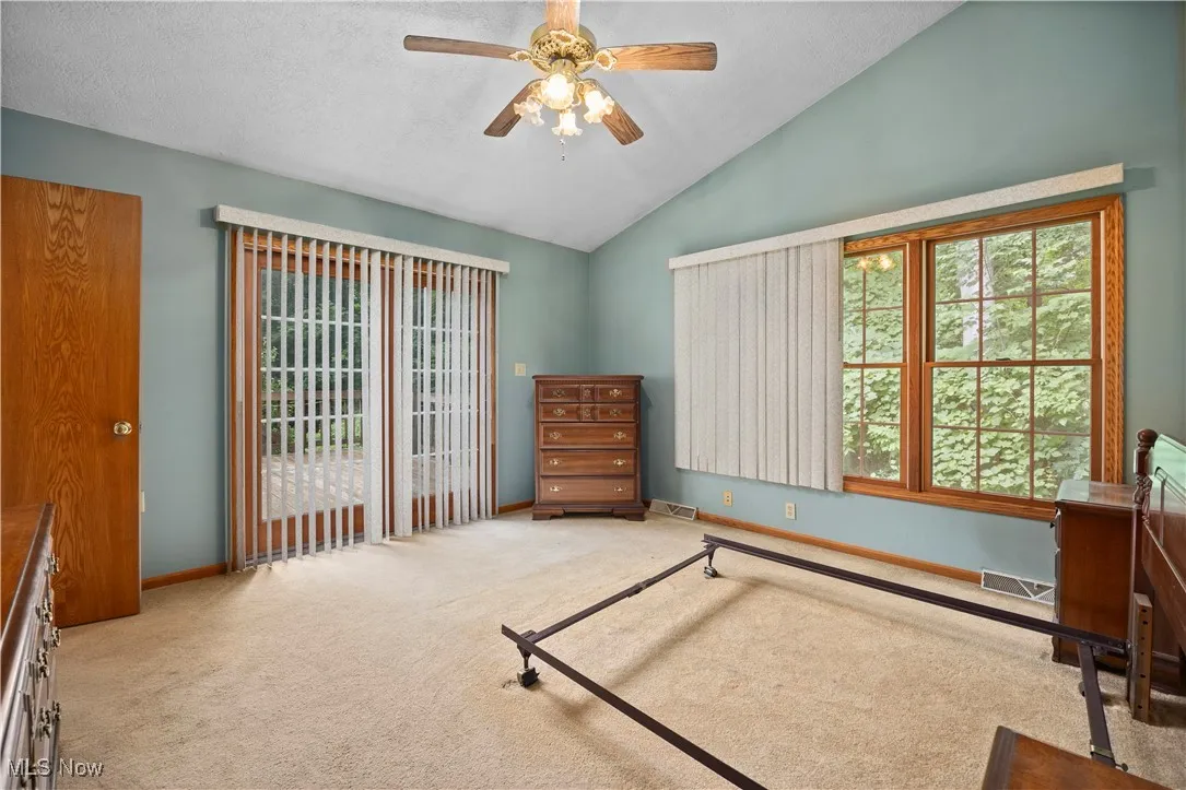 Carpeted bedroom featuring access to exterior, a ceiling fan, vaulted ceiling, and a textured ceiling