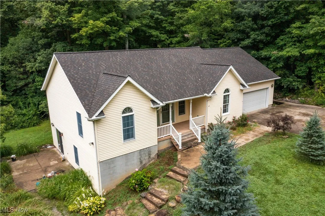 View of front of house with a shingled roof, covered porch, an attached garage, and a front lawn