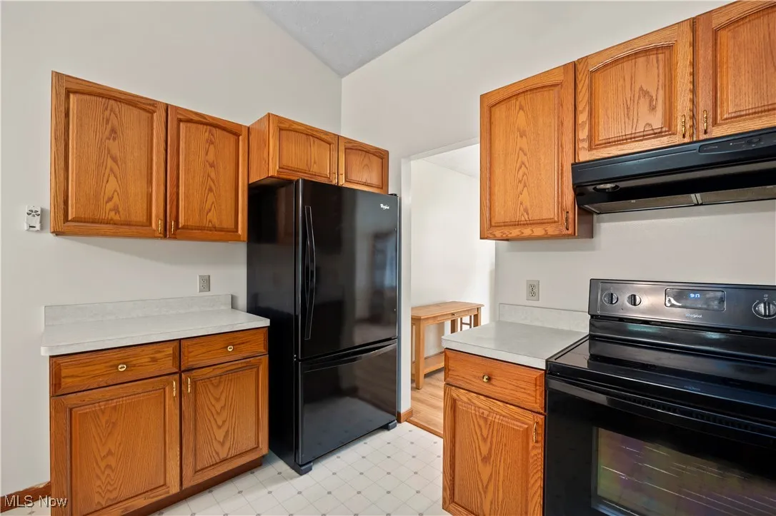 Kitchen with black appliances, under cabinet range hood, light countertops, brown cabinets, and light floors