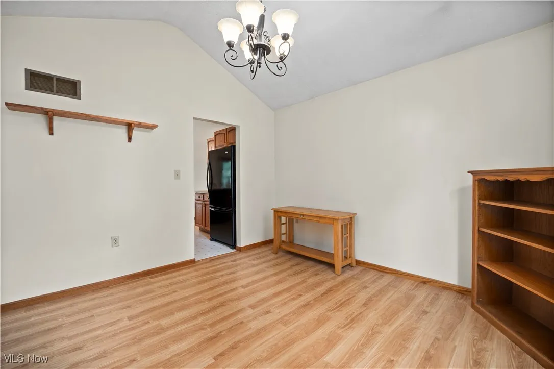 Unfurnished dining area featuring light floors, vaulted ceiling, and a chandelier