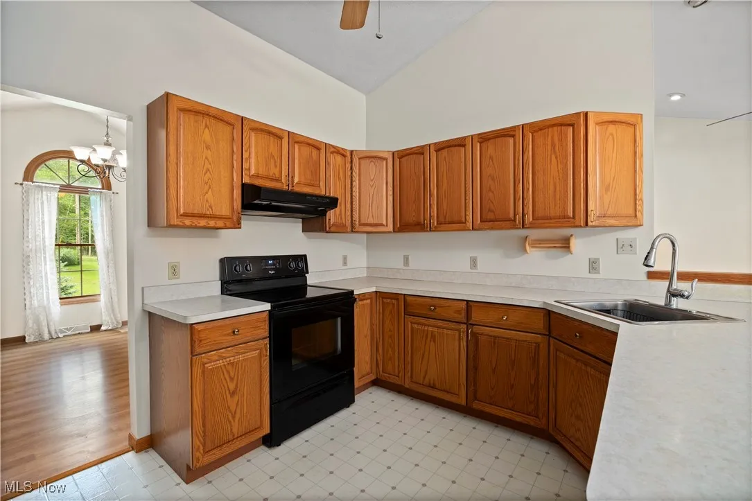 Kitchen with brown cabinetry, black range with electric stovetop, light countertops, vaulted ceiling, and under cabinet range hood