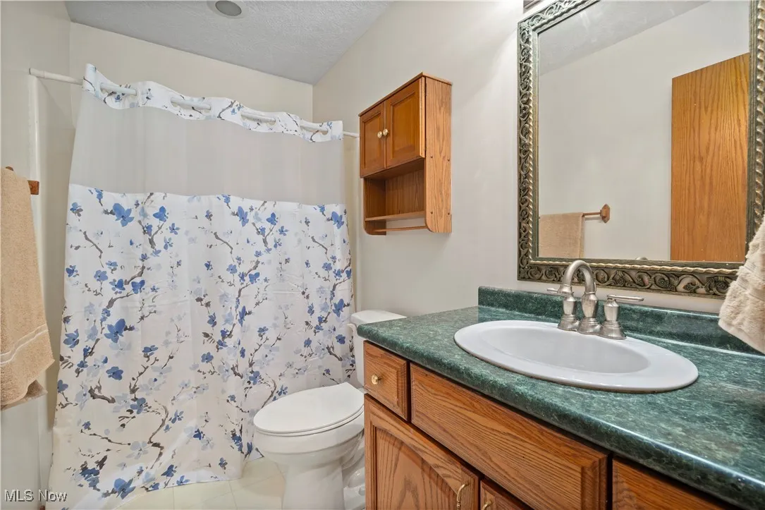 Bathroom with vanity, a textured ceiling, shower / bathtub combination with curtain, and light tile patterned floors