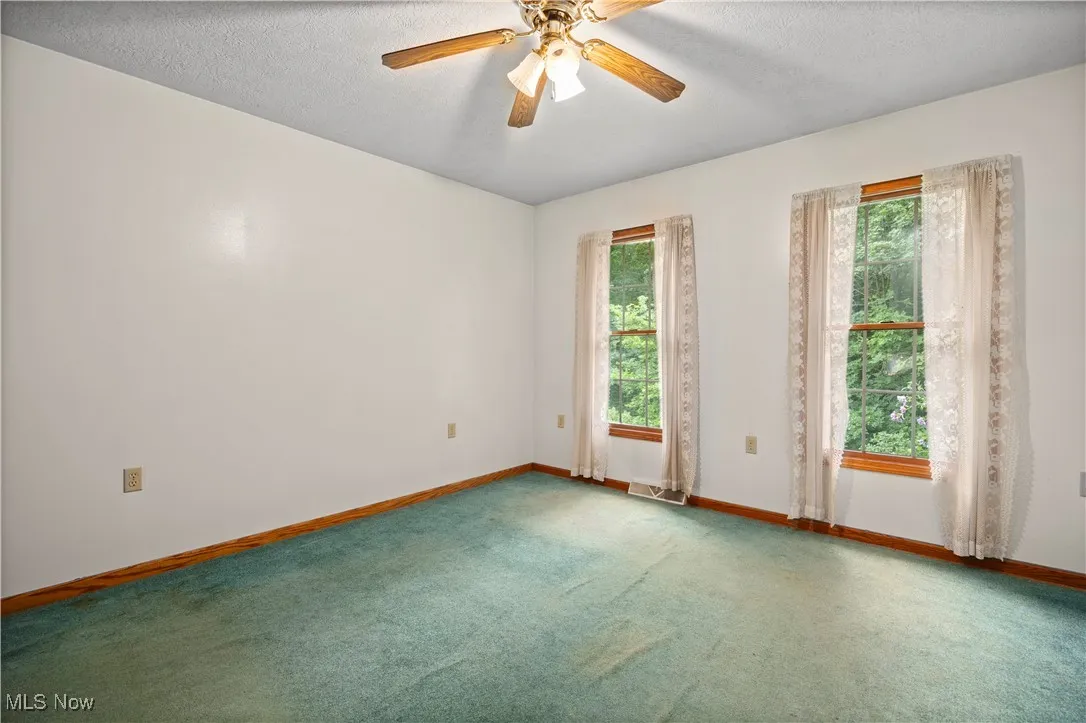 Carpeted spare room featuring healthy amount of natural light, a textured ceiling, and a ceiling fan