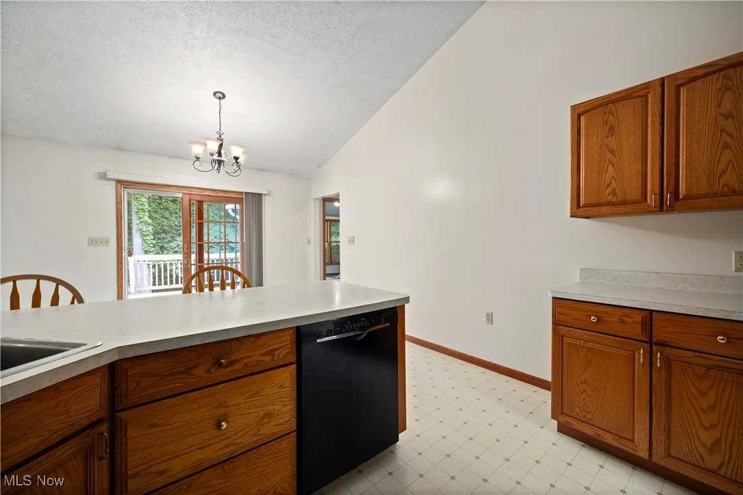 Kitchen with brown cabinetry, vaulted ceiling, light countertops, dishwasher, and a textured ceiling
