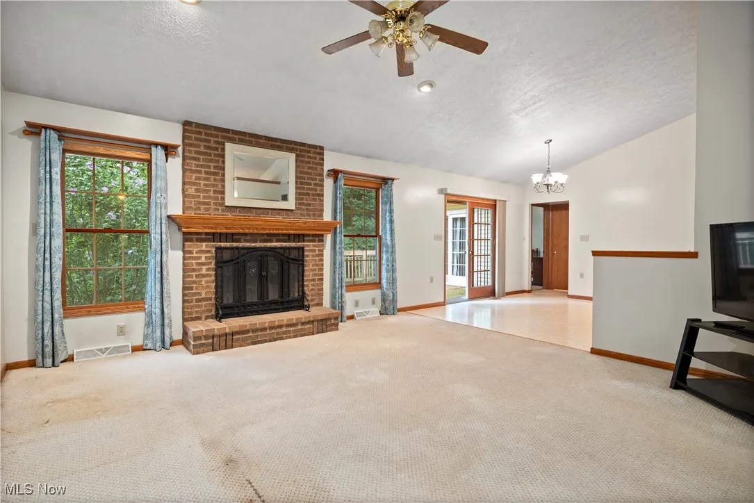 Unfurnished living room with a textured ceiling, a fireplace, carpet floors, vaulted ceiling, and ceiling fan