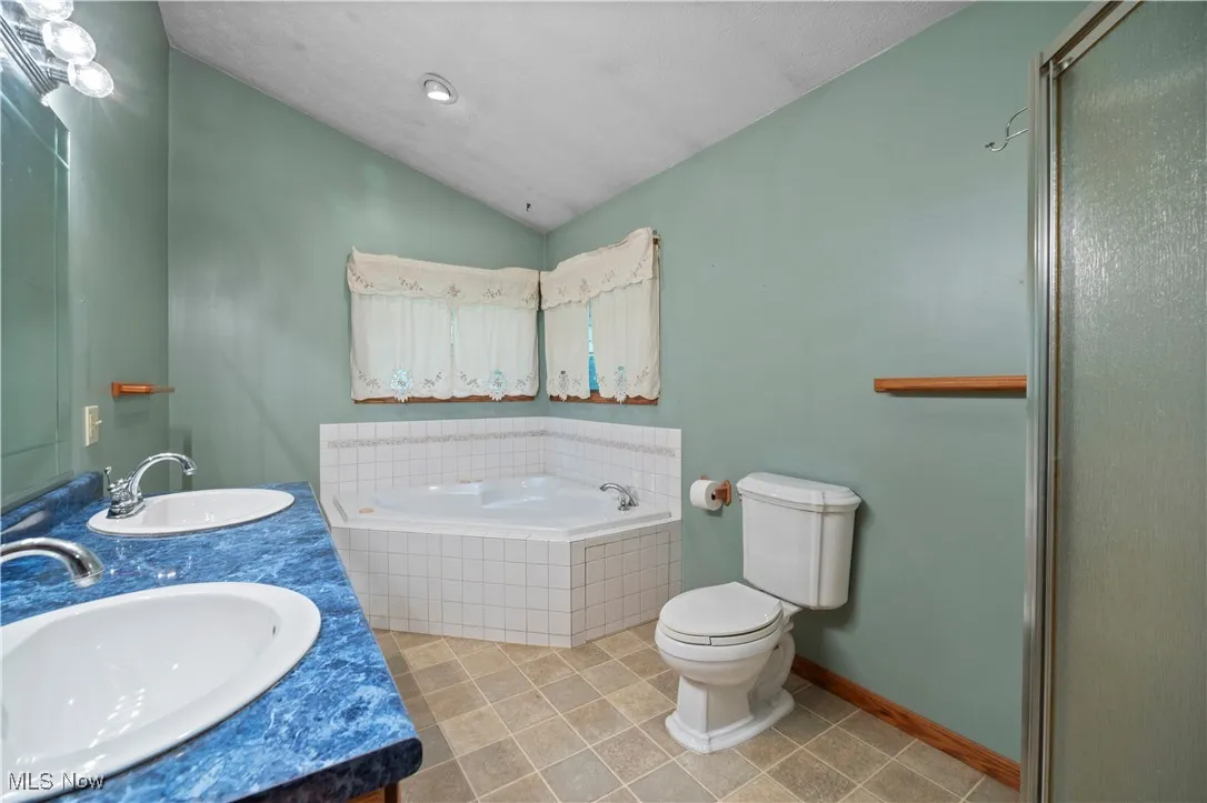 Full bath with a garden tub, vaulted ceiling, double vanity, light tile patterned flooring, and a shower stall