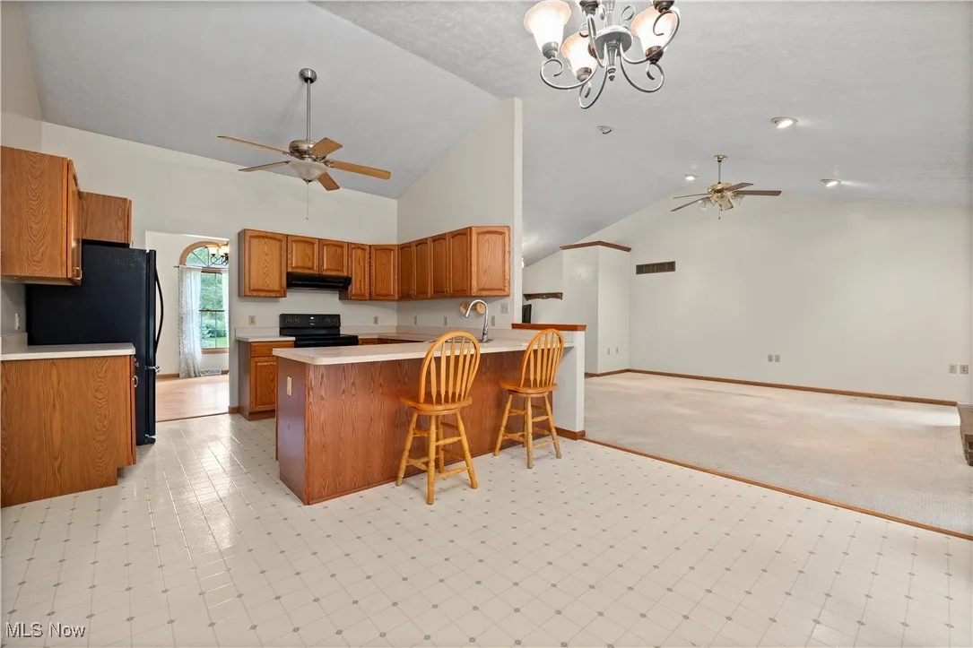 Kitchen featuring a ceiling fan, brown cabinets, a chandelier, light countertops, and high vaulted ceiling