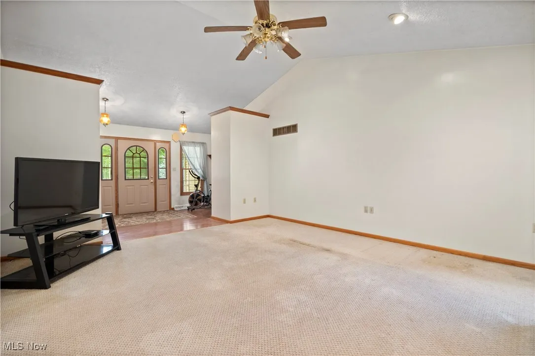 Unfurnished living room with carpet flooring, a ceiling fan, and high vaulted ceiling