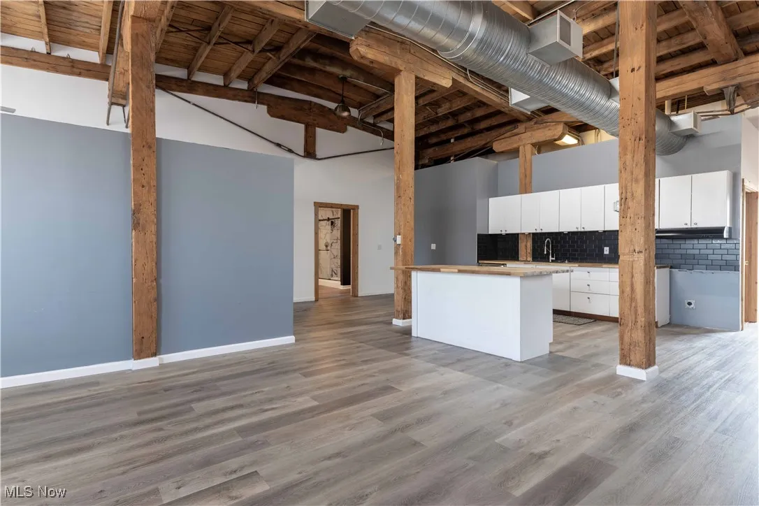 Kitchen with decorative backsplash, white cabinetry, light wood finished floors, light countertops, and high vaulted ceiling