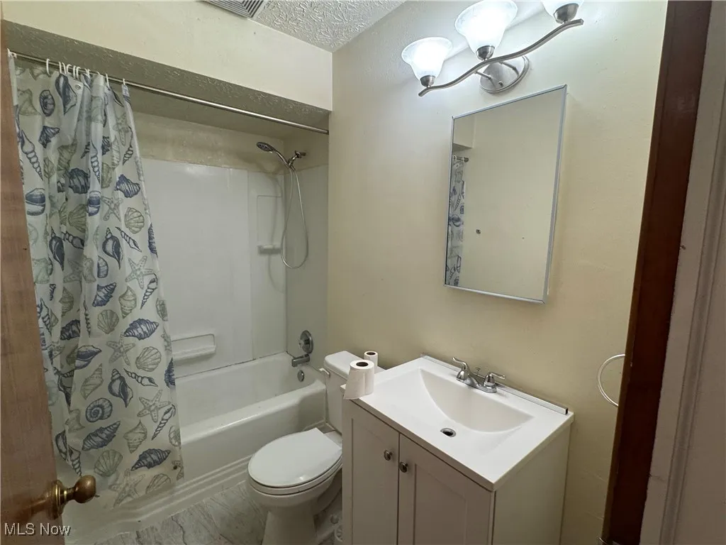 Full bath featuring a textured ceiling, vanity, and shower / bath combo