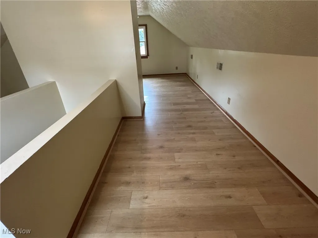 Corridor featuring a textured ceiling, light wood-style flooring, an upstairs landing, and lofted ceiling