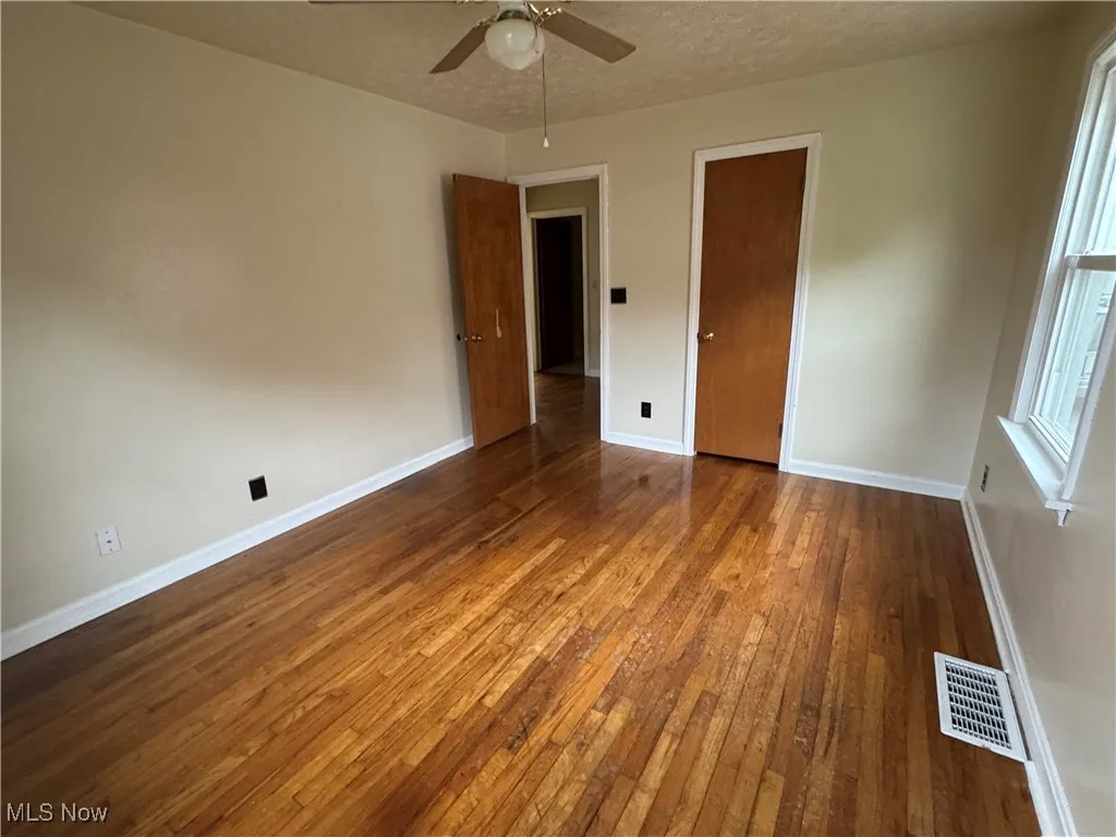 Unfurnished bedroom with hardwood / wood-style flooring, ceiling fan, and a textured ceiling