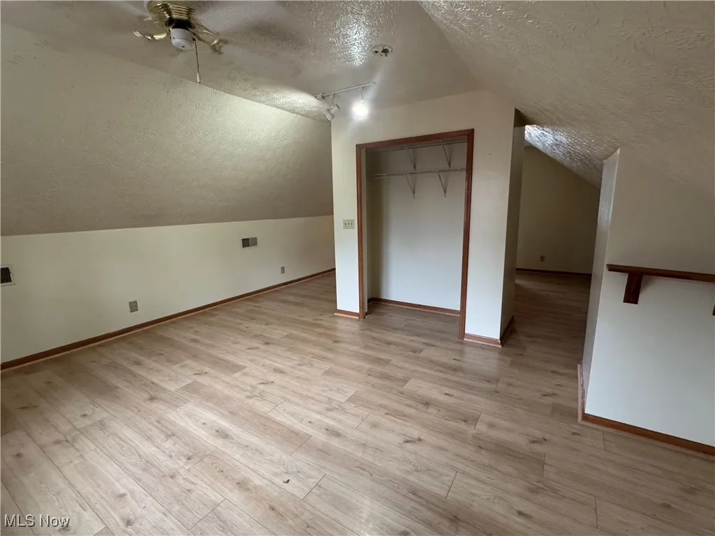 Bonus room featuring a textured ceiling, vaulted ceiling, light wood-type flooring, and ceiling fan