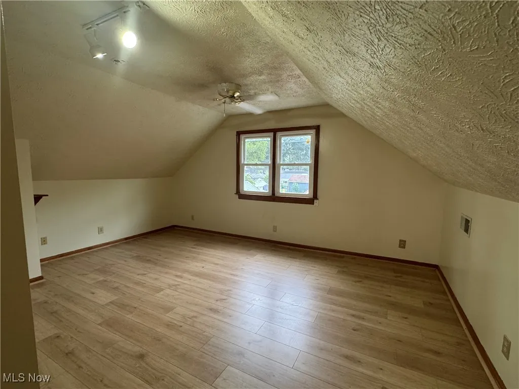 Additional living space featuring light wood-style flooring, a textured ceiling, vaulted ceiling, and a ceiling fan