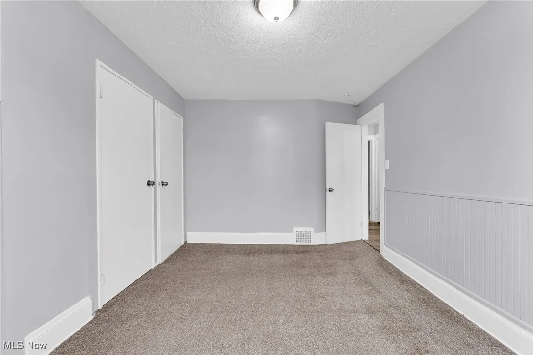 Carpeted spare room featuring a textured ceiling and baseboards