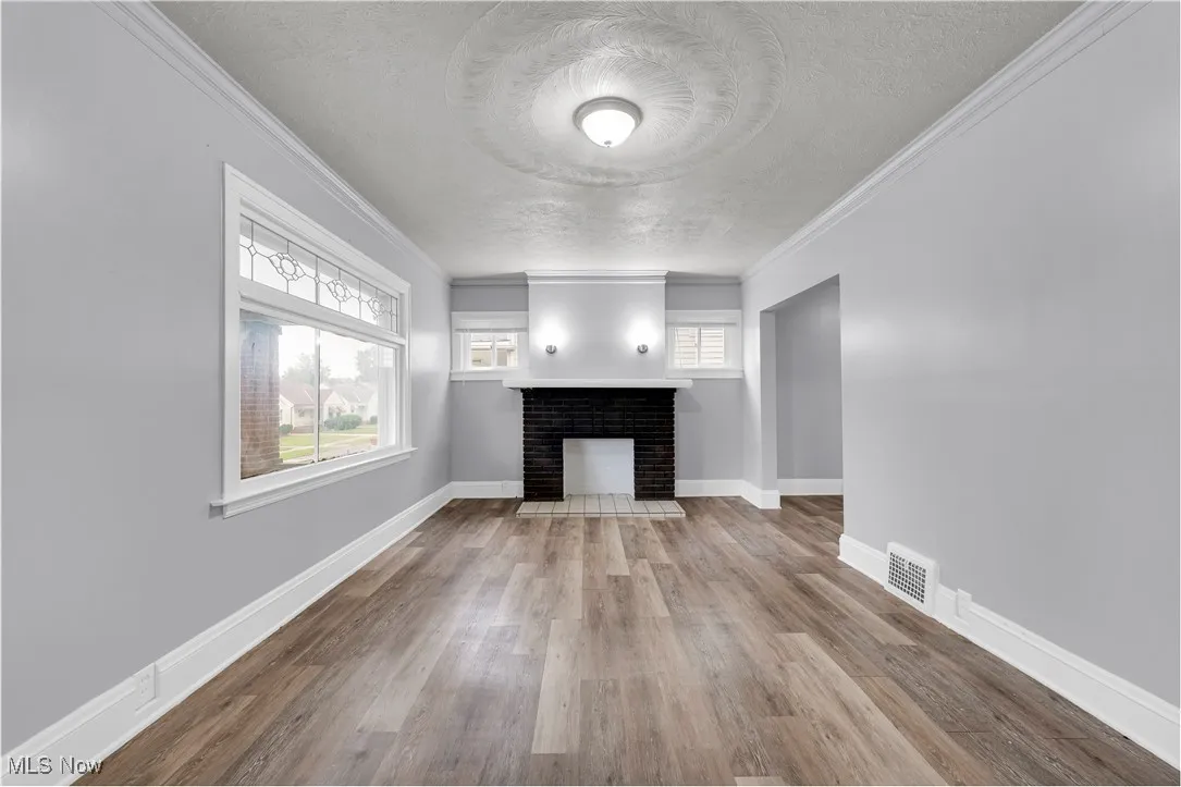 Unfurnished living room with crown molding, a textured ceiling, a brick fireplace, and light wood-style floors