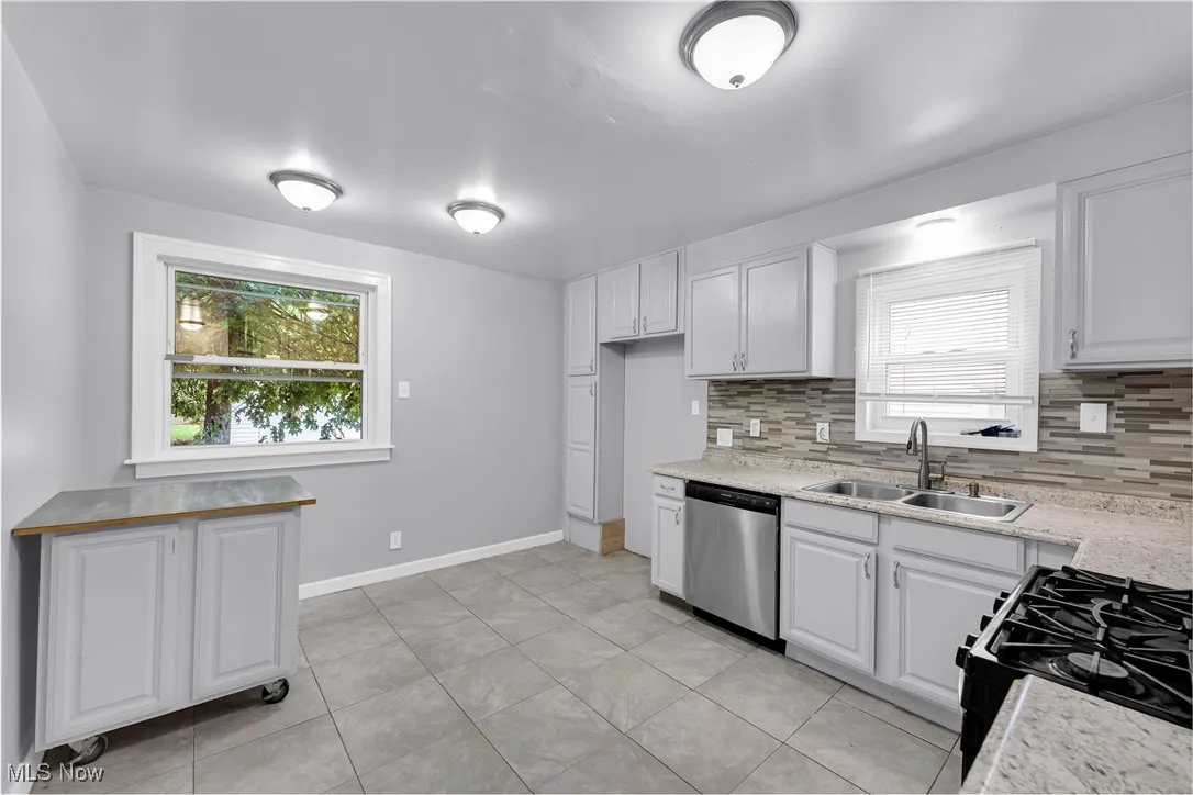 Kitchen featuring white cabinetry, black range with gas cooktop, backsplash, stainless steel dishwasher, and light tile patterned floors