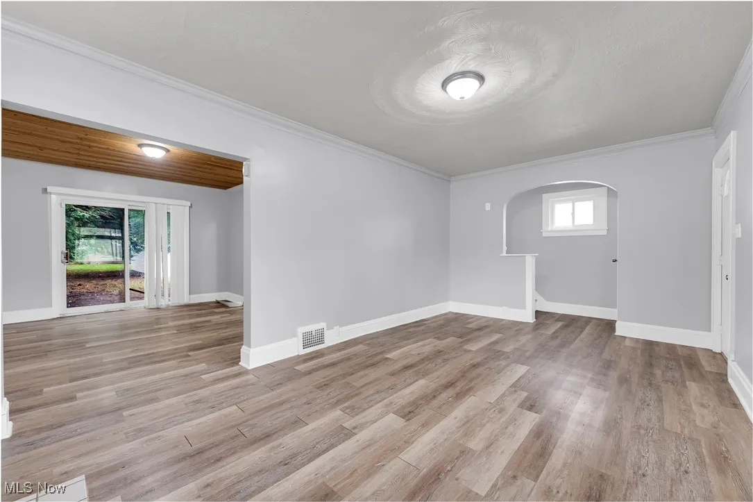 Spare room with arched walkways, ornamental molding, and light wood-type flooring