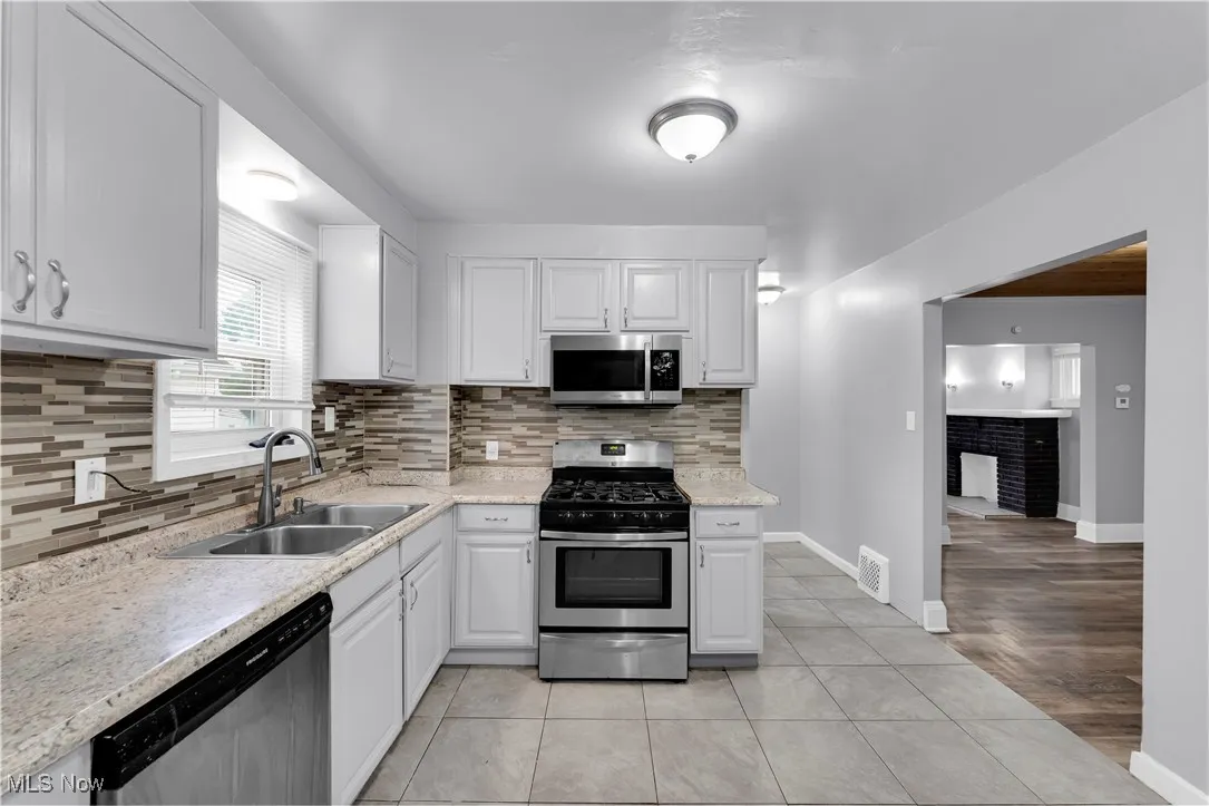 Kitchen featuring light tile patterned floors, appliances with stainless steel finishes, decorative backsplash, white cabinets, and a fireplace