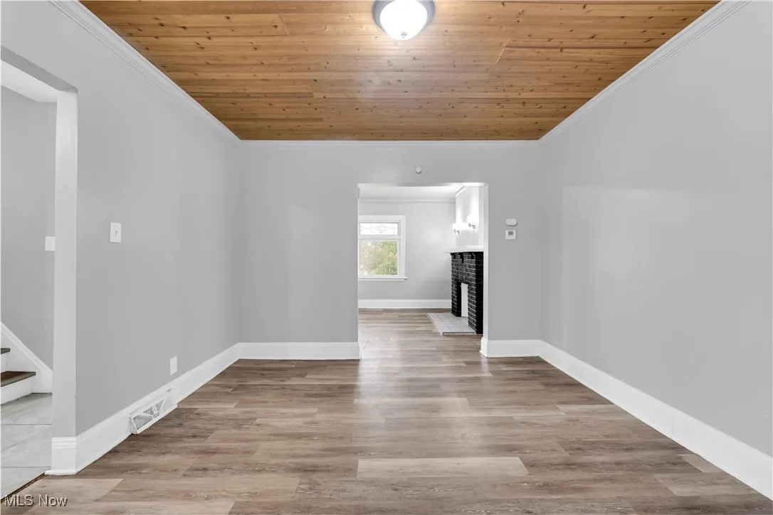 Spare room with crown molding, wood ceiling, a fireplace, light wood-style flooring, and stairway