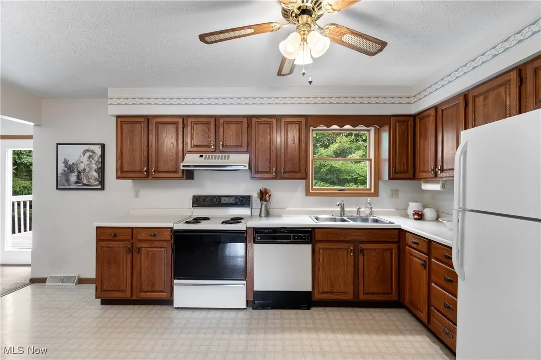 Kitchen featuring white appliances, a textured ceiling, light countertops, light flooring, and under cabinet range hood