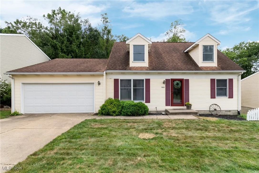New england style home with an attached garage, a shingled roof, concrete driveway, and a front lawn