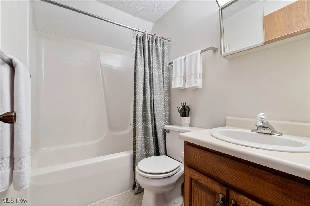 Bathroom with shower / bath combo, vanity, and a textured ceiling