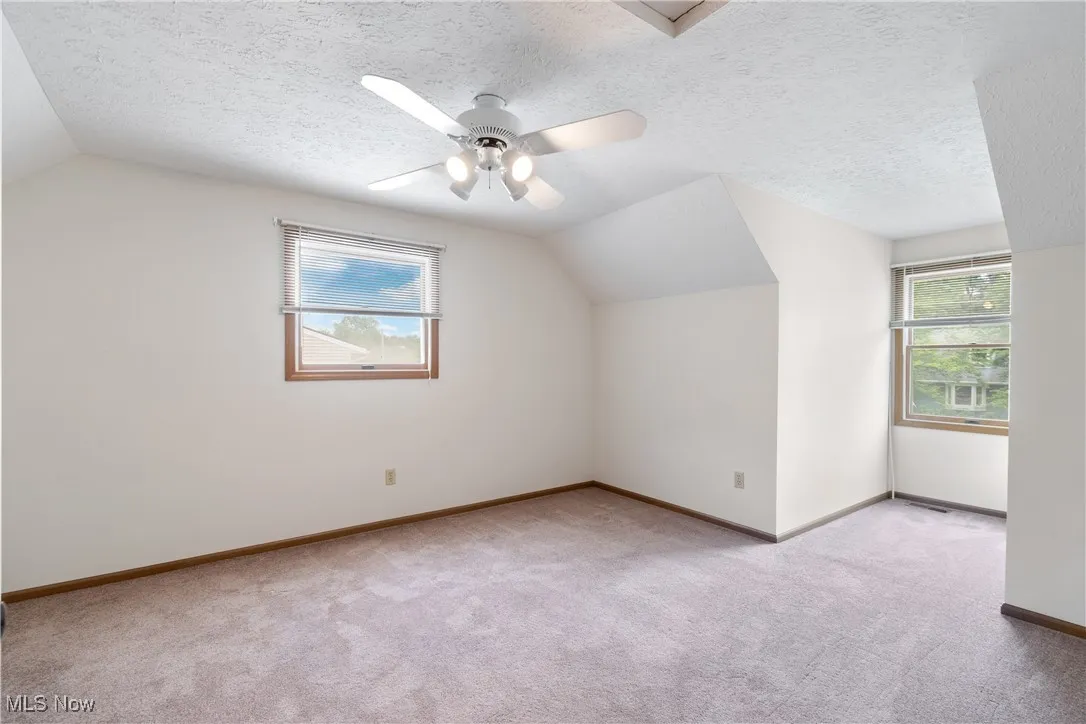 Bonus room featuring vaulted ceiling, light carpet, a textured ceiling, and ceiling fan
