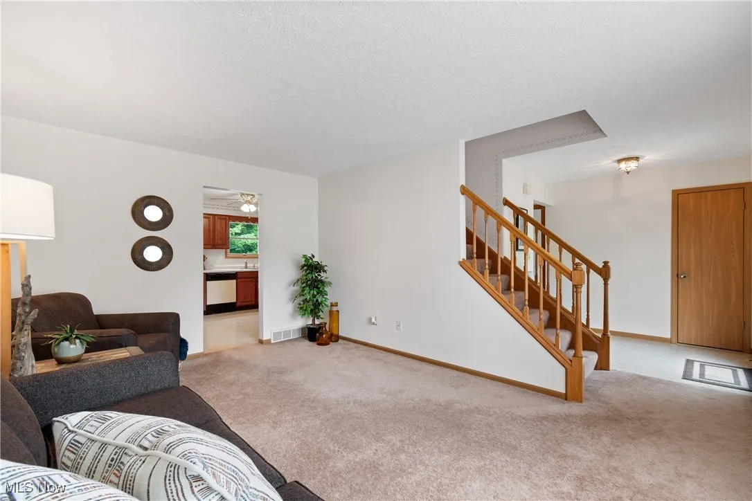 Carpeted living room with stairs, a textured ceiling, and a ceiling fan