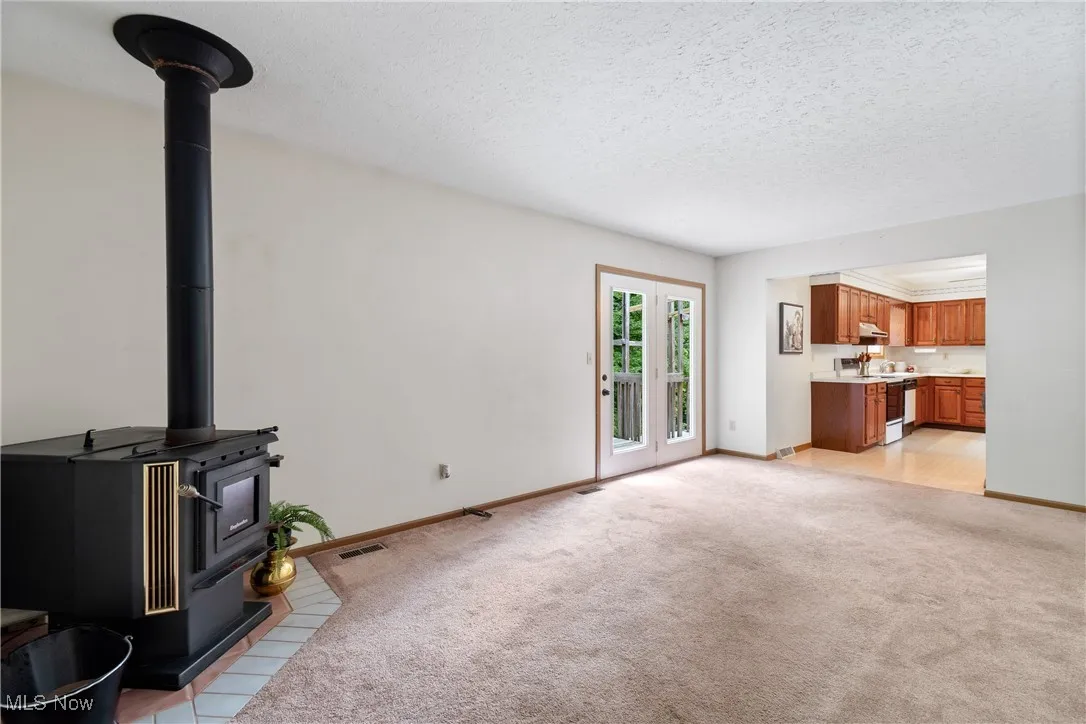 Unfurnished living room featuring a textured ceiling, light colored carpet, a wood stove, and light tile patterned floors