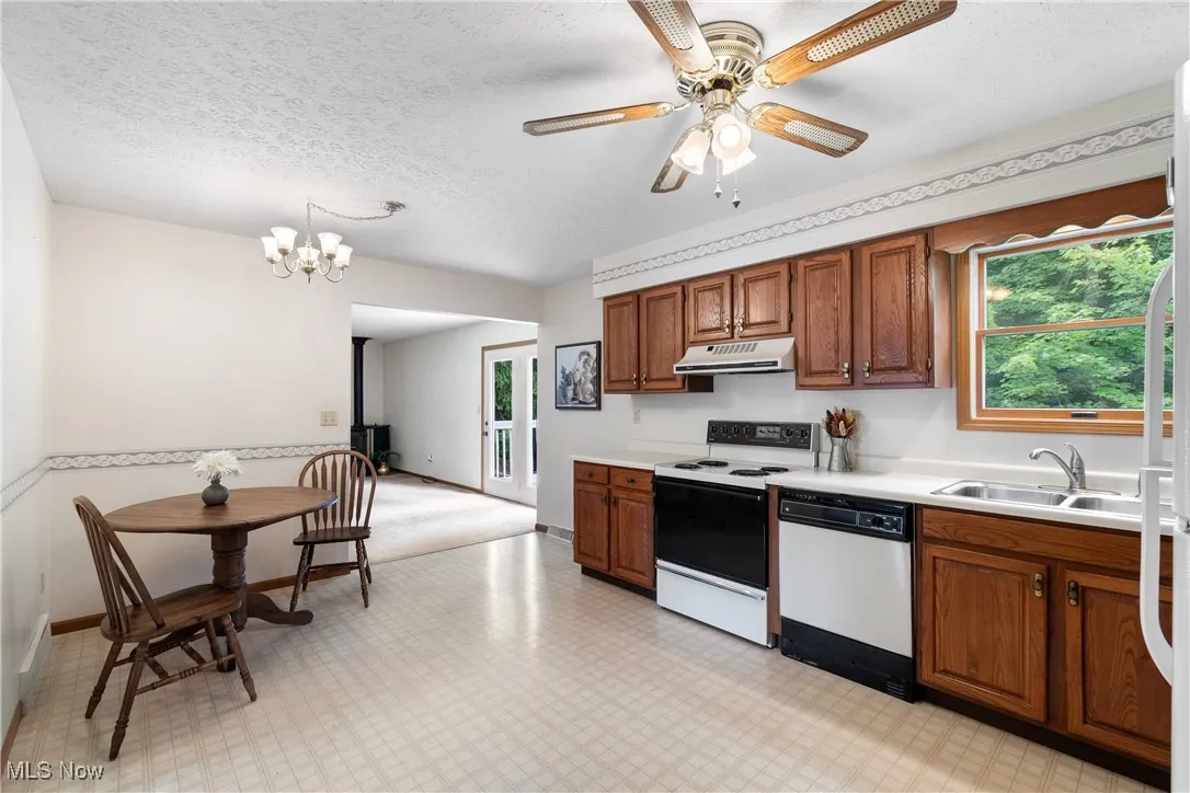 Kitchen featuring white appliances, brown cabinets, light countertops, a textured ceiling, and under cabinet range hood