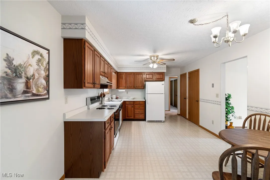 Kitchen featuring light countertops, white appliances, light flooring, brown cabinets, and a textured ceiling