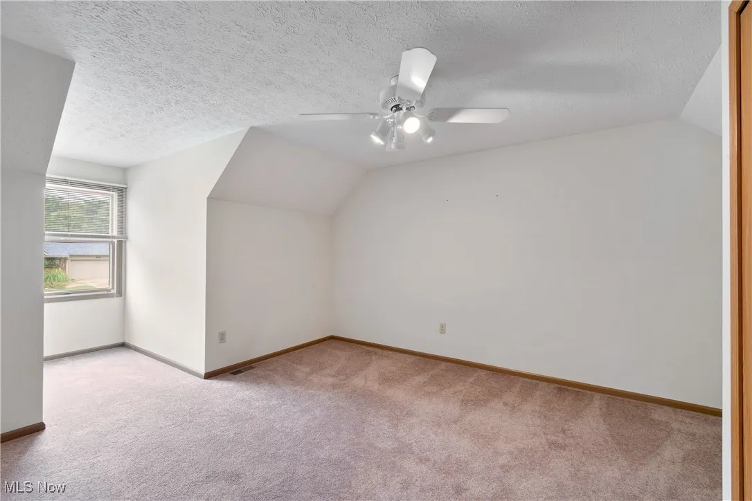 Additional living space featuring vaulted ceiling, carpet flooring, a textured ceiling, and ceiling fan