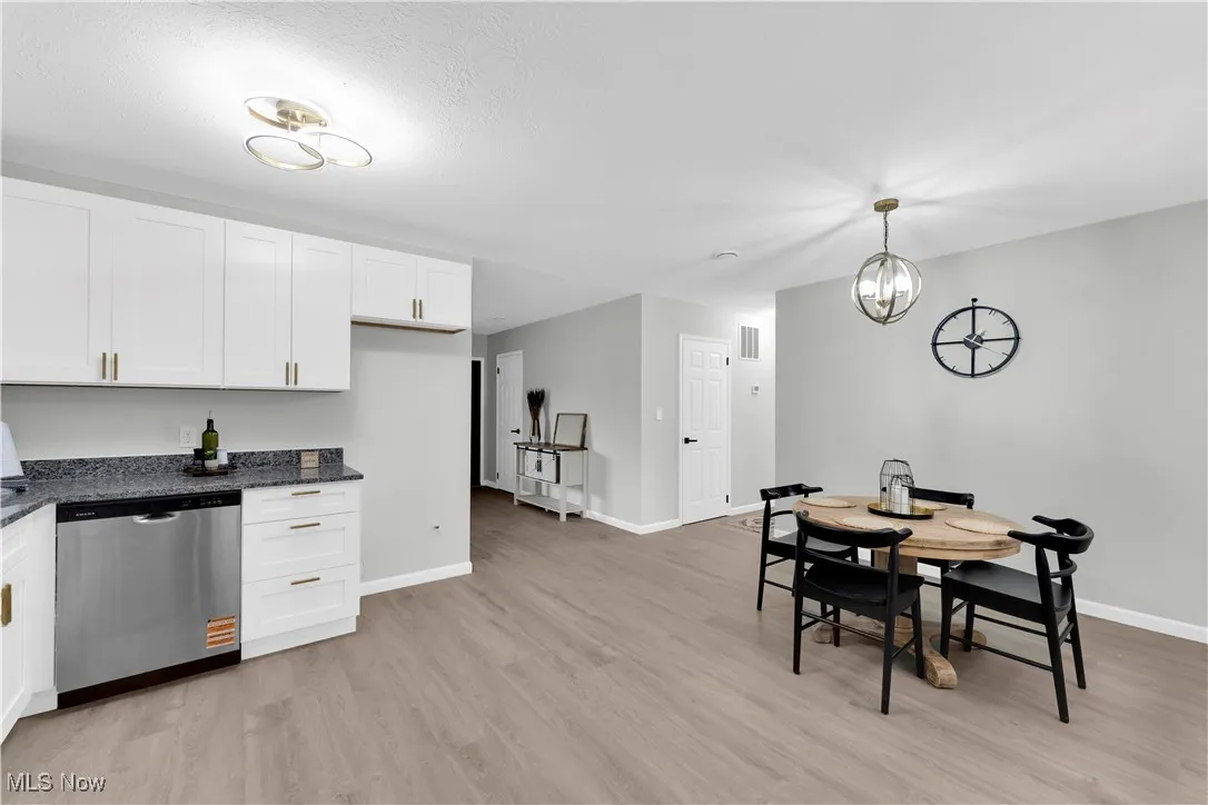 Kitchen featuring white cabinetry, stainless steel dishwasher, dark stone counters, light wood finished floors, and pendant lighting