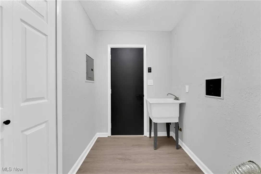 Laundry area featuring light wood finished floors, a textured wall, a textured ceiling, and electric panel
