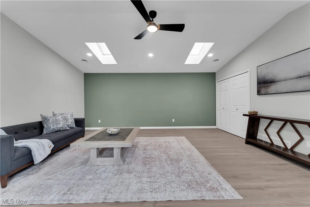 Living room with light wood-style floors, a skylight, a ceiling fan, and recessed lighting