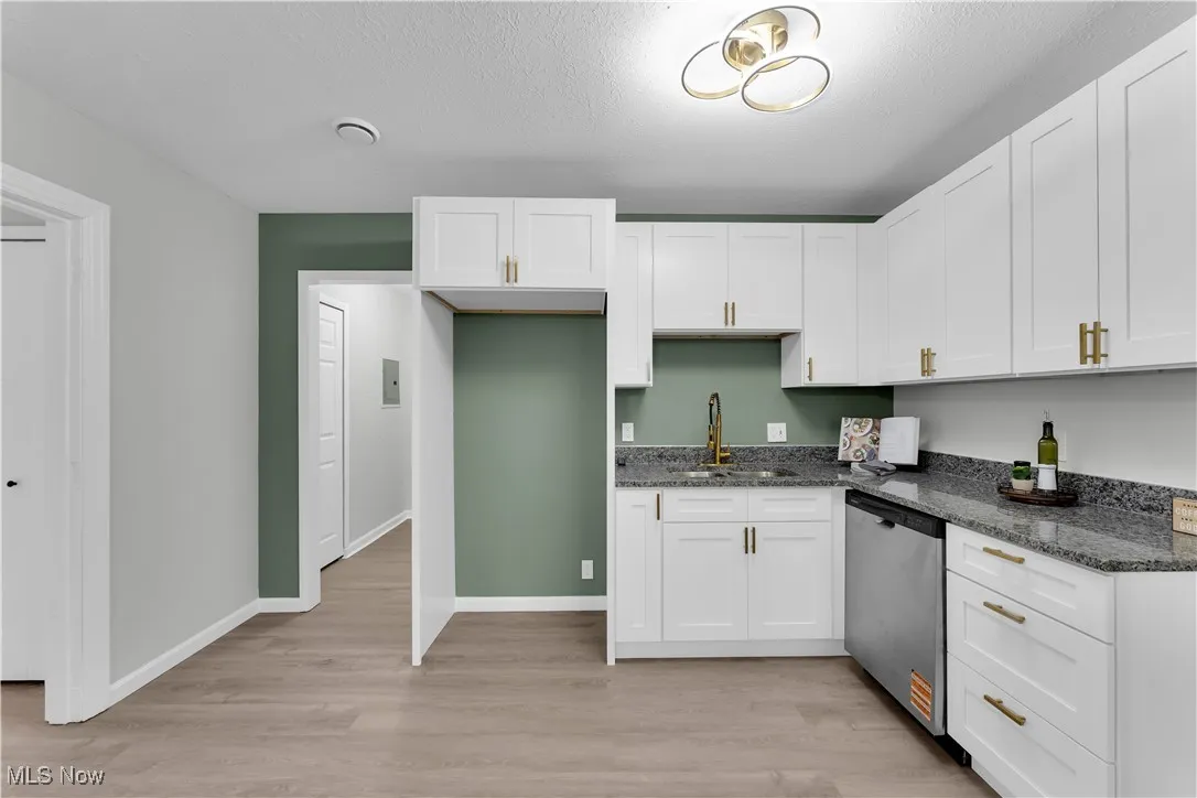 Kitchen featuring dark stone counters, stainless steel dishwasher, white cabinetry, and a textured ceiling