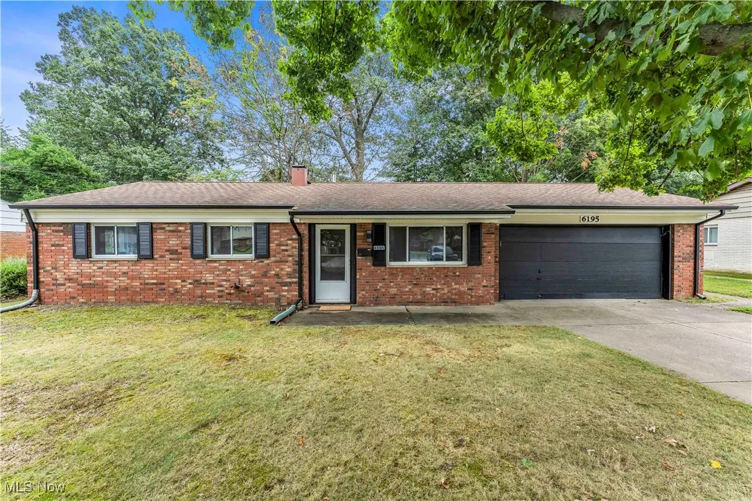 Ranch-style home featuring an attached garage, brick siding, a front lawn, a chimney, and concrete driveway